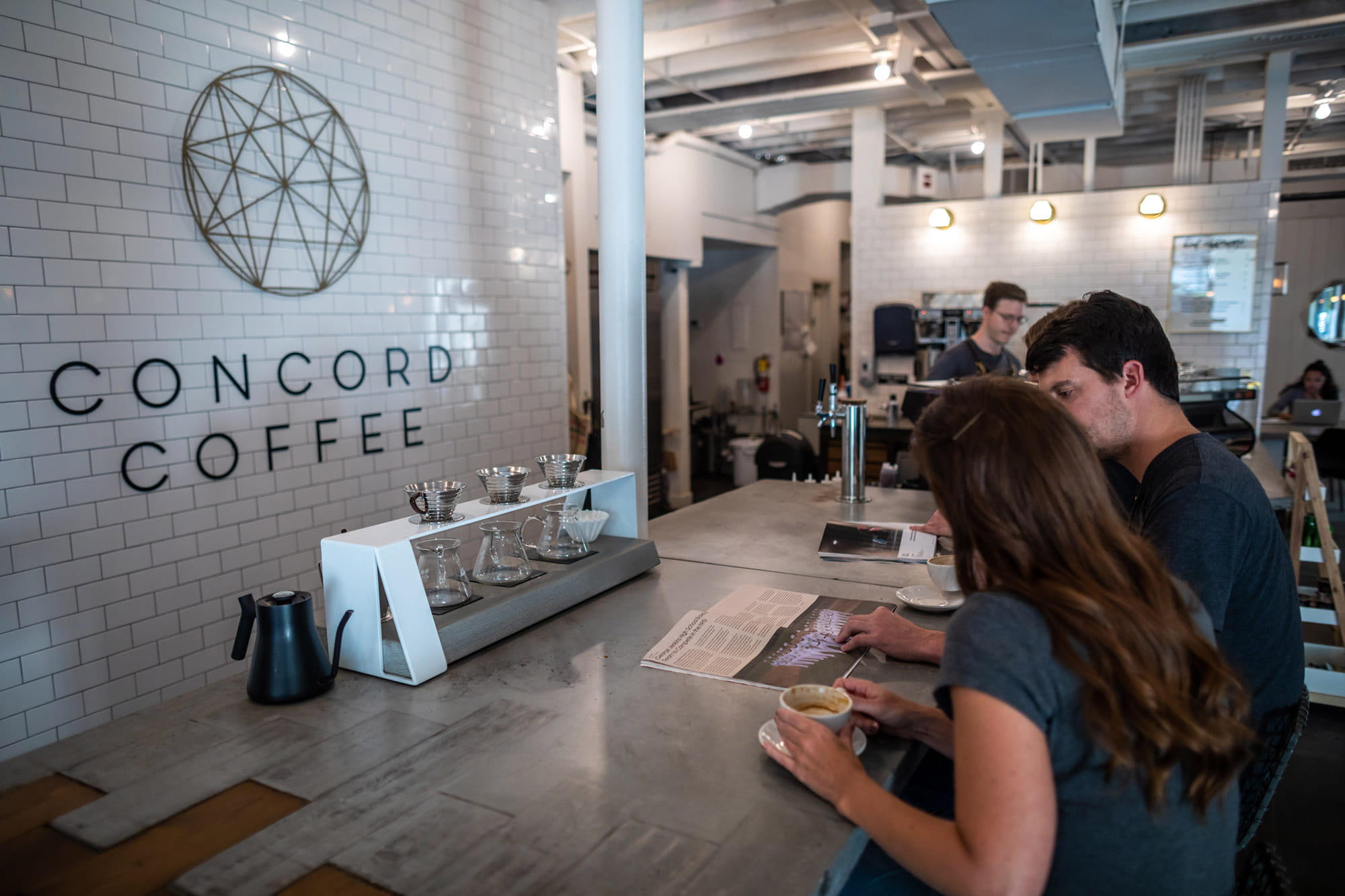 2 people sitting a coffee bar, reading magazine. Drinks are on bar. At Concord Coffee in Lakeland, FL