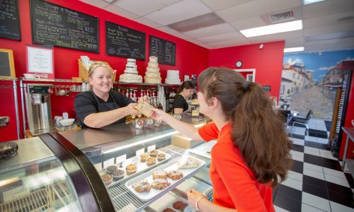 Woman handing purchased baked goods to customer over pastry filled bakery counter at Cookie Jar Bake Shop in Bartow, FL