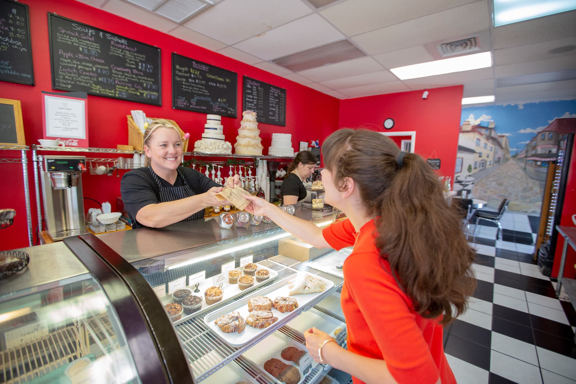 Woman handing purchased baked goods to customer over pastry filled bakery counter at Cookie Jar Bake Shop in Bartow, FL