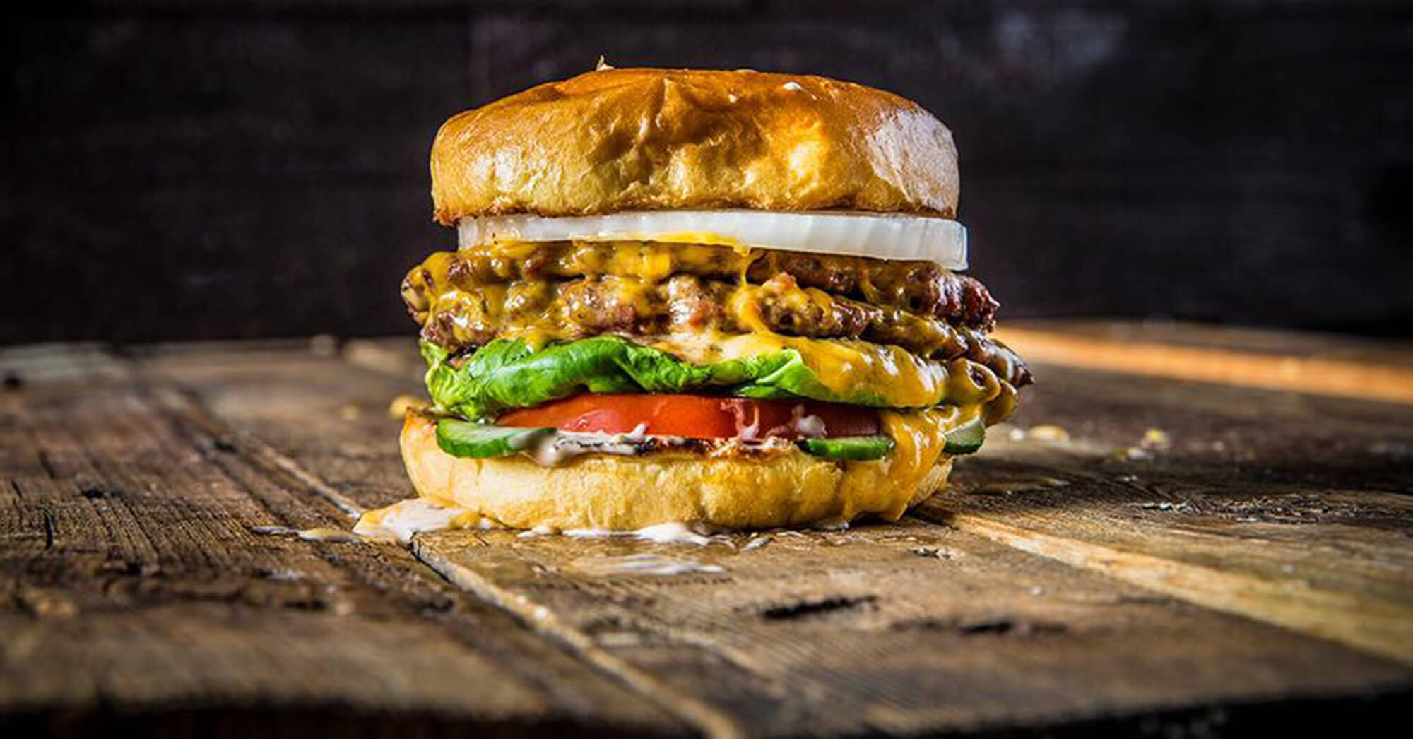 Hamburger with onion, cheese, lettuce, tomato, pickle and sauce on wooden table at Fire Restaurant in Winter Haven, FL